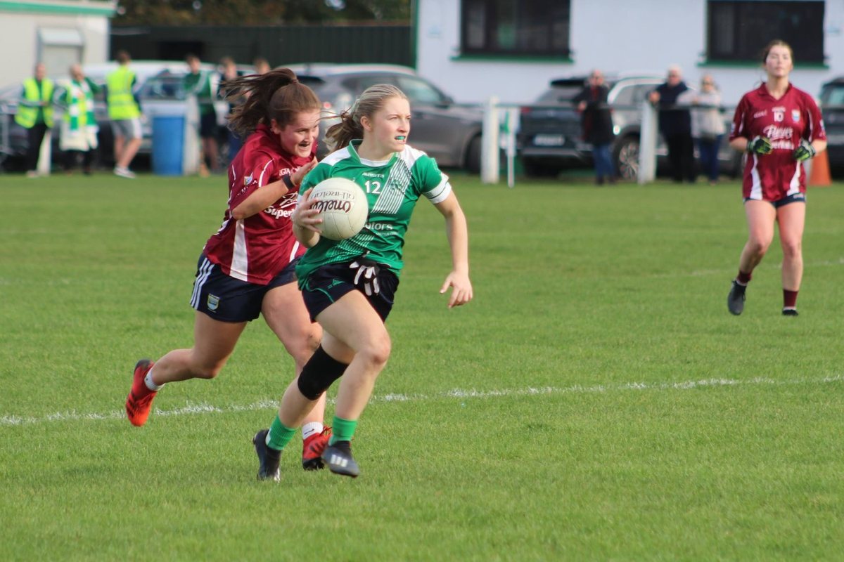 Amy Gibbons running with the ball during a ladies Gaelic football match, with an opponent chasing