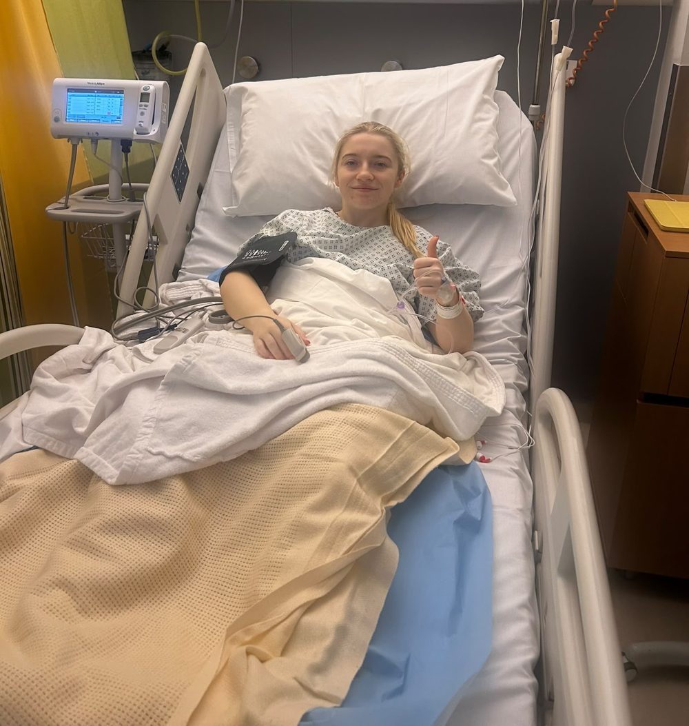 Amy Gibbons in a hospital bed giving a thumbs up after her ACL reconstruction