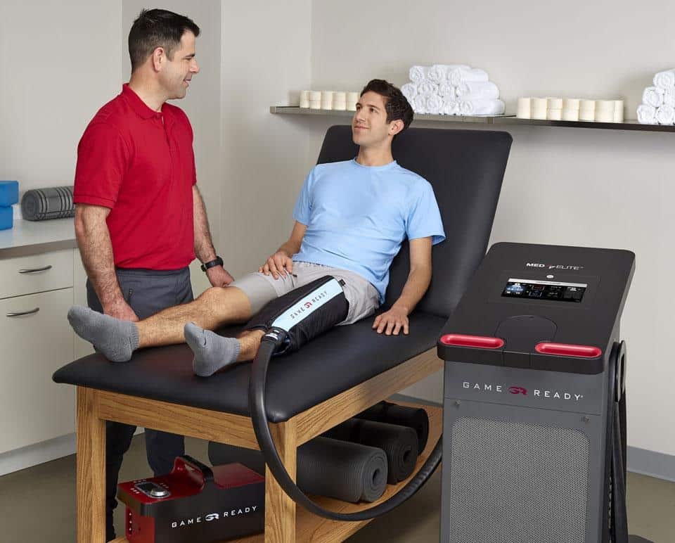 A physiotherapist with a patient using a Game Ready knee wrap connected to the Med4 Elite, with a GRPro 2.1 unit on the shelf below