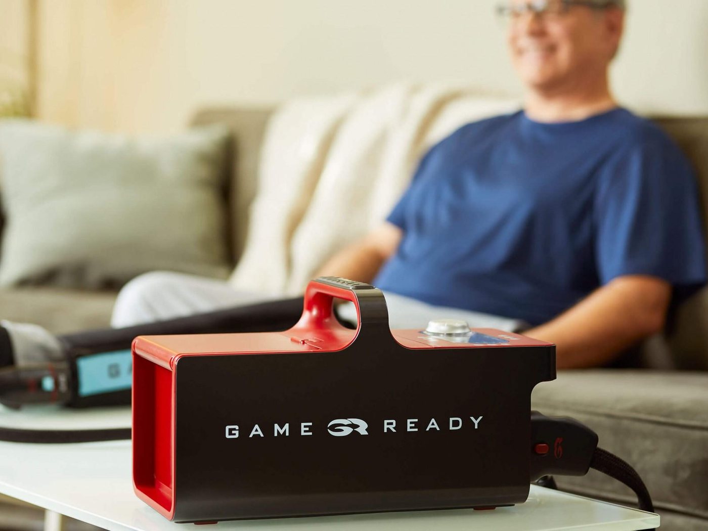 A man relaxing on his sofa at home with a Game Ready wrap on his leg and the Game Ready unit on the coffee table