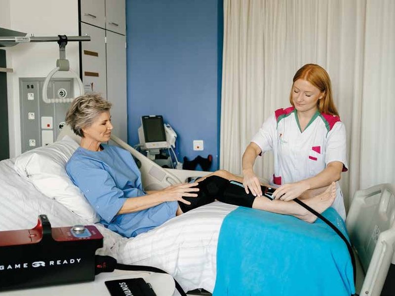A nurse fitting a Game Ready knee wrap on a patient in a hospital bed